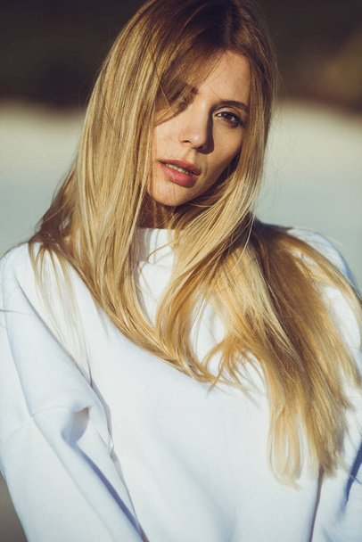 Portrét krásné blondýny. Módní žena na sobě bílé teplé oblečení venku na pláži. - Fotografie, Obrázek