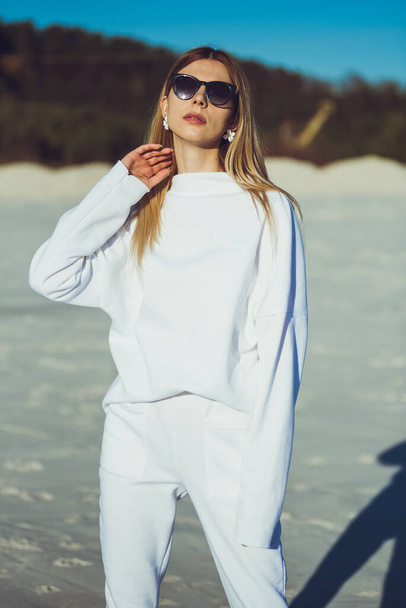 Portrait of beautiful blonde woman. Fashion woman wearing white warm clothes outdoor on the beach. - Foto, Imagem