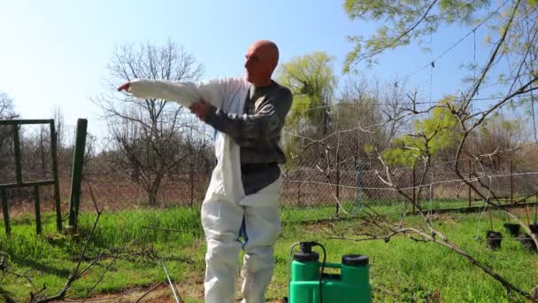 Farmer készíti védőruházatát, hogy beöltözzön a vegyi anyagok védelmére, amikor gyümölcsfákra permetez a gyümölcsöskertben, hogy megvédje őket a gombás betegségektől vagy férgektől. 4K MINDEN I - Felvétel, videó