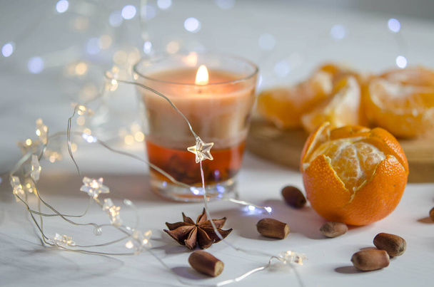 Tangerines, candle, spice and garland on a blurred background. Christmas decorations - 写真・画像