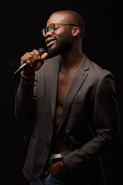 Ένας μαύρος Αφροαμερικανός τραγουδάει συναισθηματικά σε μικρόφωνο. Κοντινό πλάνο πορτρέτο στούντιο. - Φωτογραφία, εικόνα