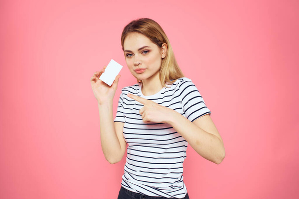 Woman with a business card in her hands a striped T-shirt pink background Copy Space advertising - Zdjęcie, obraz