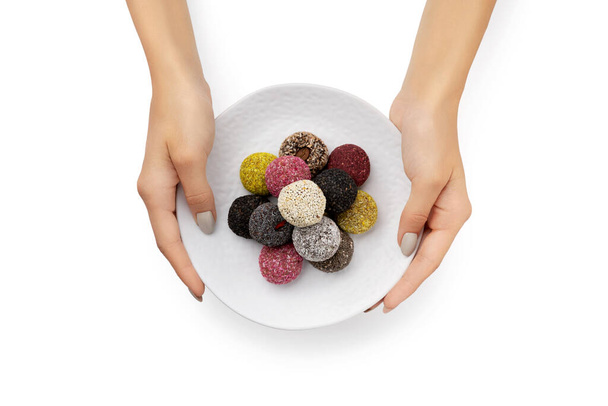 Barevné veganské bonbóny energetické koule na talíři s ženské ruce izolované bílé pozadí - Fotografie, Obrázek