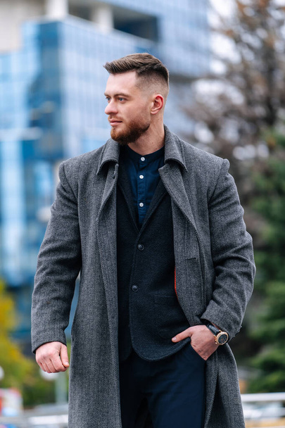 Young businessman is posing outdoor with a strong expression.Male in gray coat and dark suit. - Fotografie, Obrázek