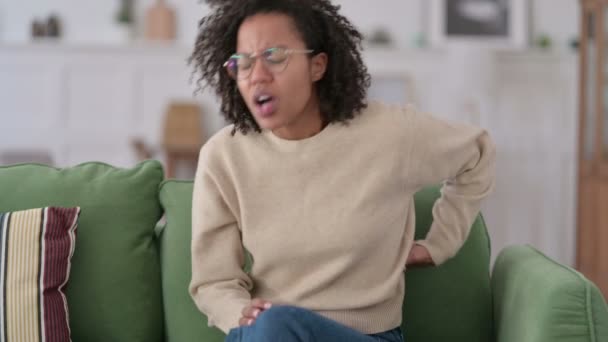 Mujer joven africana con dolor de espalda sentada en un sofá  - Imágenes, Vídeo