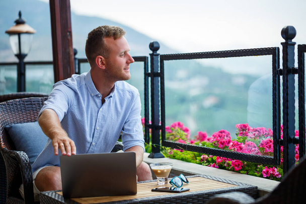 Homme d'affaires prospère travaillant en vacances derrière un ordinateur portable avec une vue sur la montagne. Flux de travail en ligne gestionnaire. Travailler à l'extérieur avec une belle vue depuis le balcon - Photo, image