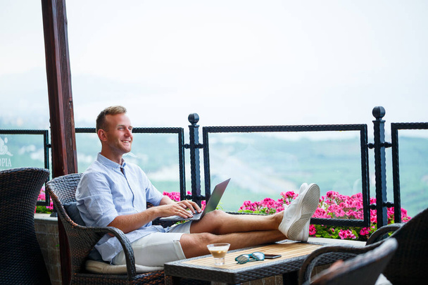 Succesvolle mannelijke zakenman werkend op vakantie achter een laptop met uitzicht op de bergen. Werkstroom van online managers. Buiten werken met een prachtig uitzicht vanaf het balkon - Foto, afbeelding