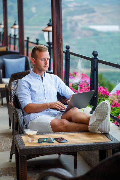 Homem de negócios bem sucedido trabalhando em férias atrás de um laptop com vista para a montanha. Fluxo de trabalho do gerente online. Trabalhe ao ar livre com uma bela vista da varanda - Foto, Imagem