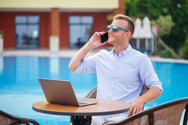 Jeune homme d'affaires avec ordinateur portable assis près de la piscine. Lieu de travail ouvert. Concept de pigiste. Achats en ligne. Travaux de vacances - Photo, image