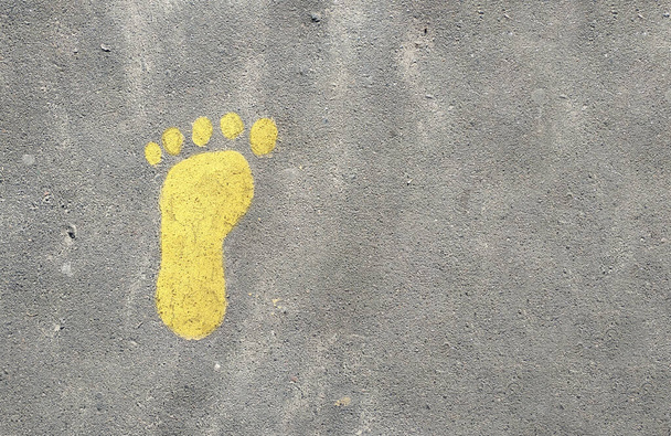 Żółty malowany odcisk stopy na szarym tle asfaltu. Widok z góry - Zdjęcie, obraz