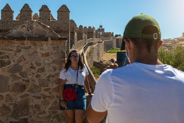 selektivní zaměření chlapce fotografujícího dívku na vrcholu zdi pevnosti Avila ve Španělsku v letním dni - Fotografie, Obrázek