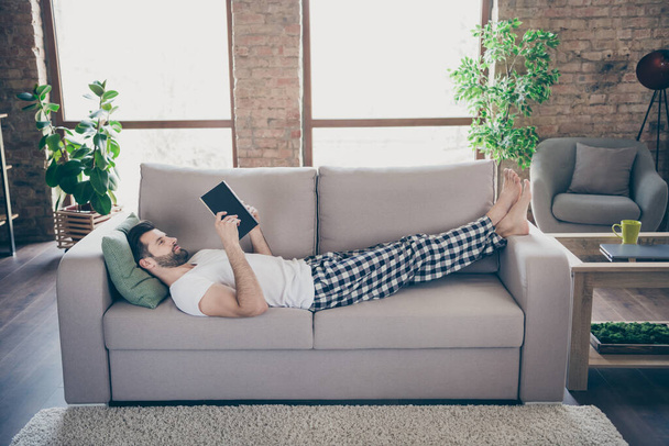 Profile photo of domestic homey handsome guy stay home quarantine reader book worm good mood lying comfy cozy sofa modern interior living room apartments indoors - Foto, imagen