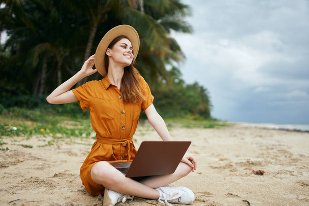 donna con computer portatile vicino all'oceano sull'isola sulla sabbia  - Foto, immagini