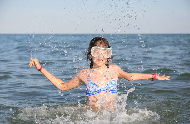 νεαρά κορίτσια φορούν μαγιό και μάσκα κατάδυσης και παίζουν ψεκάζοντας θαλασσινό νερό στον αέρα το καλοκαίρι - Φωτογραφία, εικόνα