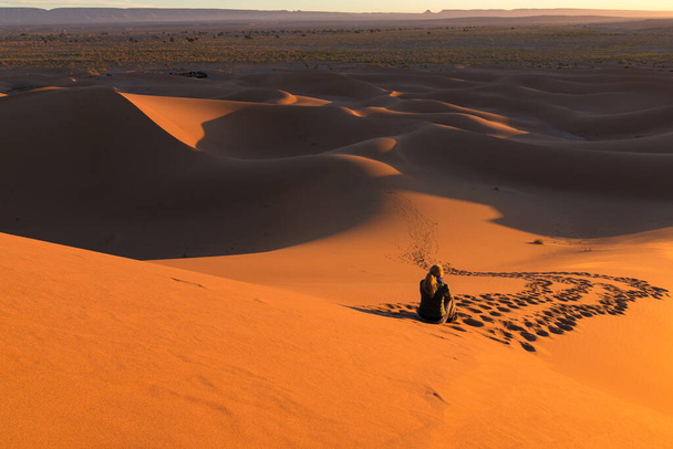 Kątowe ujęcie nierozpoznawalnej samotnej kobiety na pustynnych wydmach Erg Chigaga, u bram Sahary, o wschodzie słońca. Maroko. Pojęcie podróży i przygody - Zdjęcie, obraz