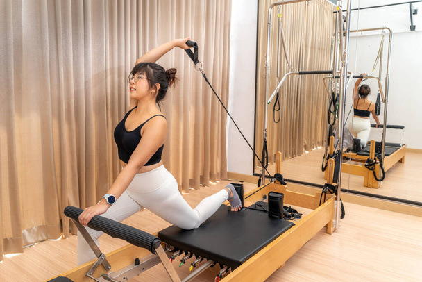 Junge Asiatin arbeitet während ihres Gesundheitstrainings an einem Pilates-Reformer - Foto, Bild