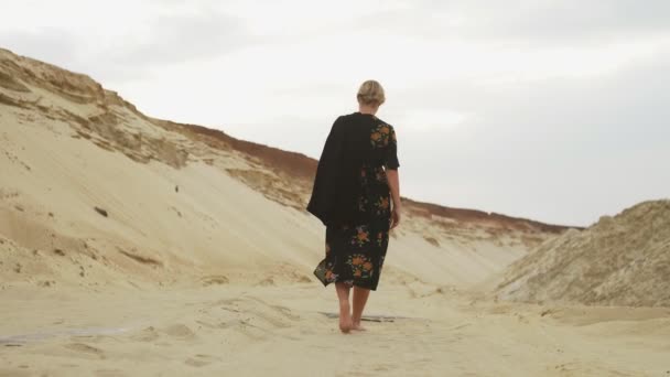 Vissza kilátás mezítlábas nő fekete ruhában sétál a sivatagban - Felvétel, videó
