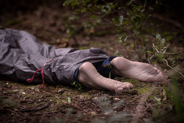 Barefoot dead body in the woods. Murder victim lying on the ground in the forest - Photo, Image