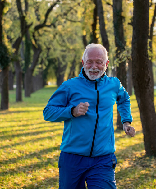 Zadowolony starszy pan biegający w parku w słoneczny jesienny dzień. Koncepcja zdrowego stylu życia - Zdjęcie, obraz