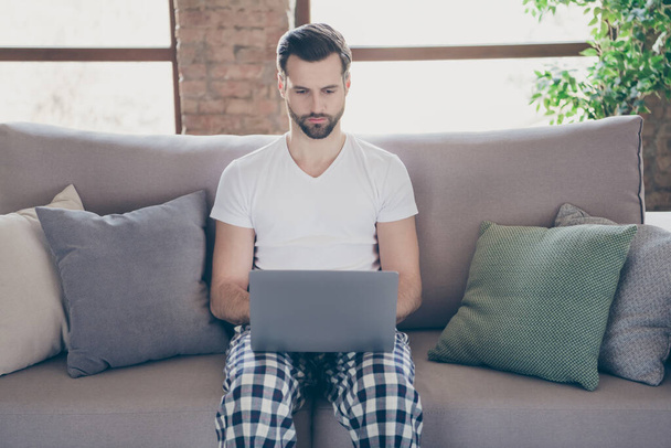 Portrait of concentrated ceo worker man sit sofa work remote laptop have online communication start-up progress online conversation colleagues partners boss sleep night wear indoors room - Foto, Imagem