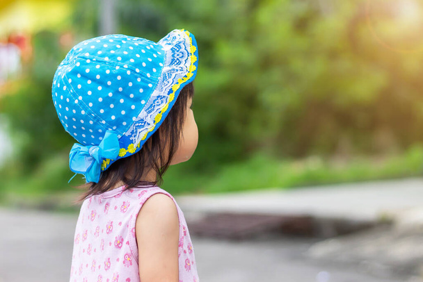 Portrét 1-2 let starého dítěte. Šťastné asijské dítě dívka stojící v zahradním parku se sluncem v letní sezóně. Má na sobě modrý klobouk a růžové šaty.. - Fotografie, Obrázek