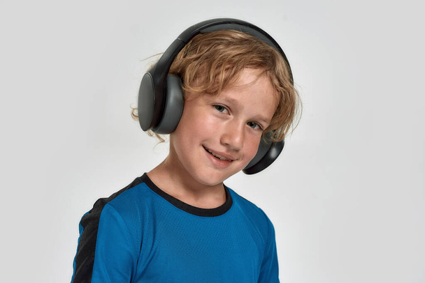 Portrait of happy little sportive boy child in sportswear and headphones smiling at camera while posing, standing isolated over white background - 写真・画像
