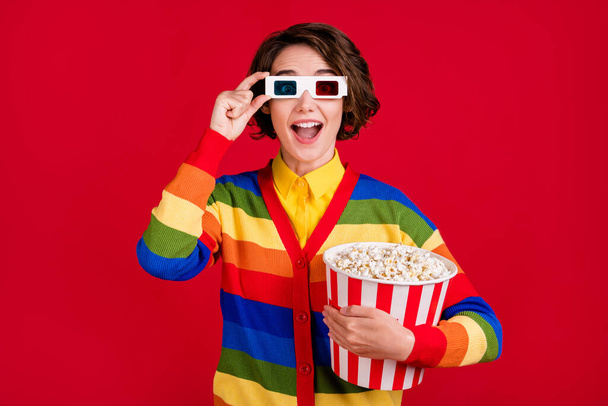 Photo of pretty funny lady hold big popcorn bucket watch movie cinema premiere nice picture quality wear 3d spectacles striped cardigan jumper isolated bright red color background - Фото, зображення