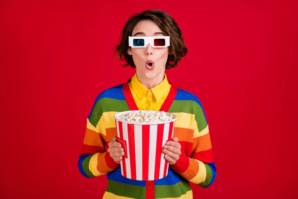 Photo of pretty shocked lady hold hands big popcorn bucket watch movie cinema thriller premiere wear 3d spectacles striped cardigan jumper isolated bright red color background - Фото, зображення