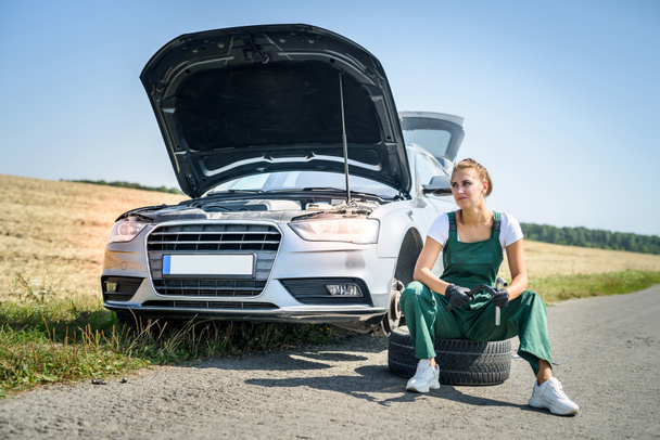 Женщина, работающая со сломанным колесом своей машины, ждет помощи - Фото, изображение