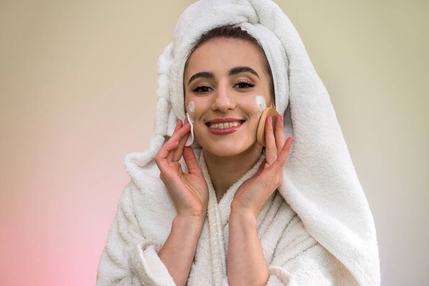 Kaunis nuori nainen kylpytakissa ja pyyhkeessä suihkun jälkeen käyttää kermanaamiota yöllä. kauneuden ja terveyden käsite - Valokuva, kuva