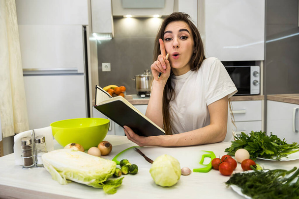 Молода жінка готує їжу, використовуючи блокнот як допомогу на своїй кухні
 . - Фото, зображення