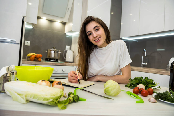 Młoda kobieta gotowanie żywności za pomocą notatnika jako pomoc w jej kuchni . - Zdjęcie, obraz