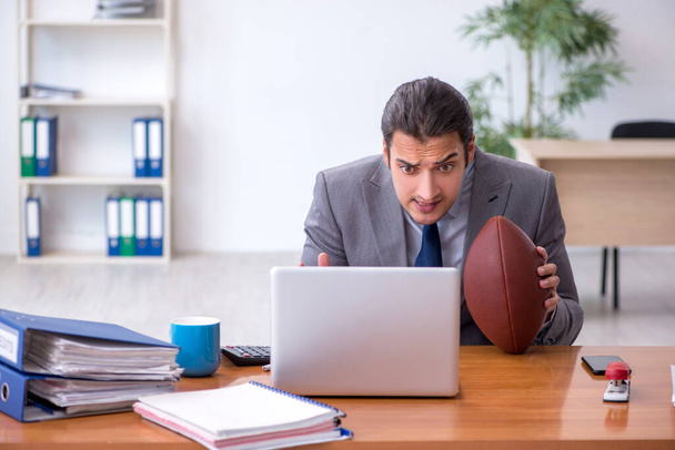 Joven empleado masculino con pelota de rugby en la oficina - Foto, Imagen