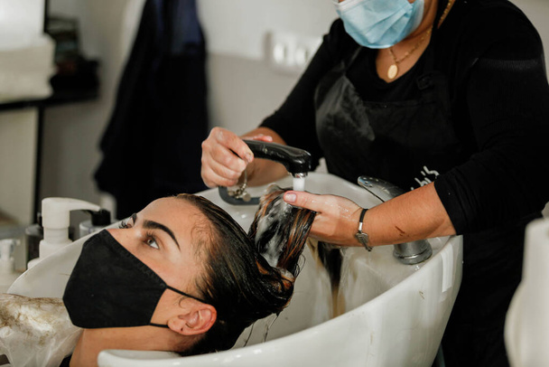 Mulher com máscara facial recebendo um estilo fresco em um salão de cabeleireiro. Mulher a lavar o cabelo, conceito de cabeleireiro. Cabeleireiro corte e styling uma mulher em sua loja - Foto, Imagem