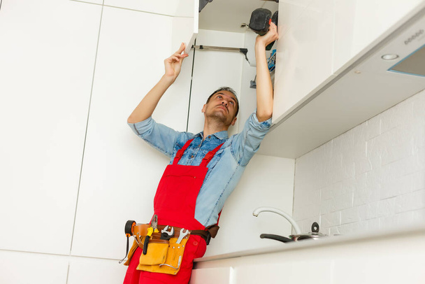 Handyman fixing kitchen's cabinet with screwdriver - 写真・画像