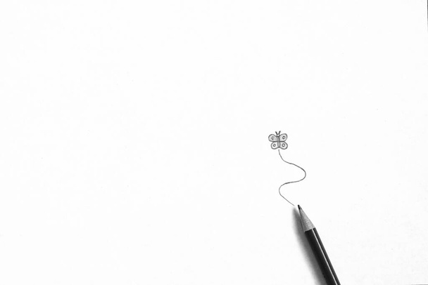 Egy minimalista absztrakt fekete-fehér közelkép egy rajzolt pillangóról fehér alapon, egy rajzceruzával alatta.. - Fotó, kép