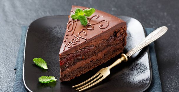 Chocolate Austrian dessert Sacher with apricot jam and mint leaves. - Photo, Image