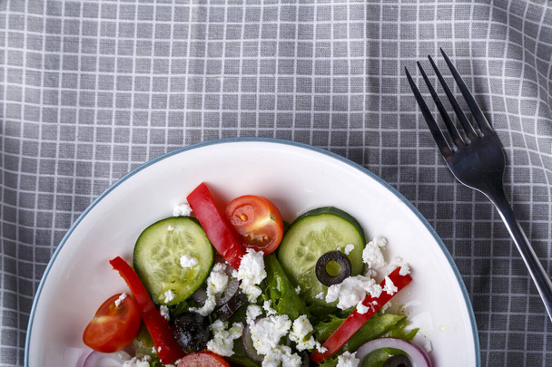 Half a light plate of Greek salad on a checkered napkin with a fork. Horizontal photo - Photo, Image