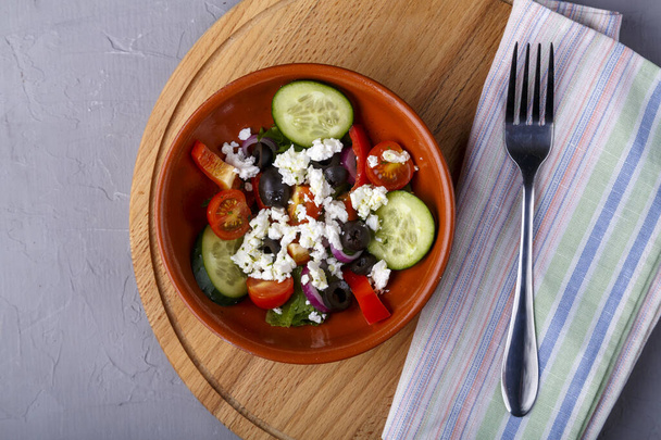 beige plate of Greek salad on a gray background on a gray napkin with a fork. Horizontal photo - Φωτογραφία, εικόνα