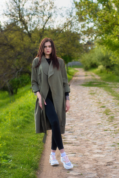 Confident girl walking in city park. Young woman in grey coat. Street lifestyle - Φωτογραφία, εικόνα