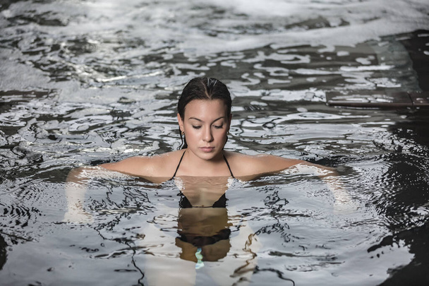 Alto ángulo de tranquila joven hermosa hembra flotando en agua cristalina de la piscina de spa durante la sesión de hidroterapia en el club de bienestar - Foto, Imagen