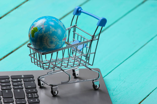Global online supermarket. Shopping trolley with globe on laptop keyboard - Fotó, kép