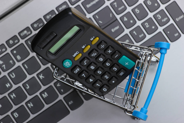Berekening van de kosten van online aankopen. Winkelwagentje met calculator op toetsenbord - Foto, afbeelding