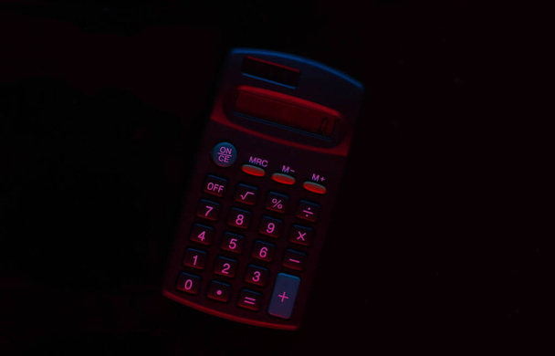Calculator with neon red-blue light on a black background. - Foto, Imagen