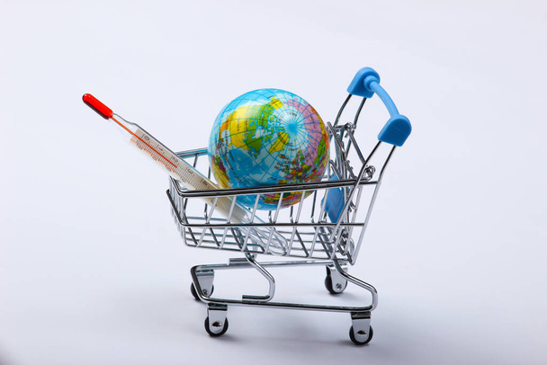 Global warming concept. Shopping trolley with globe and thermometer on a white background - 写真・画像