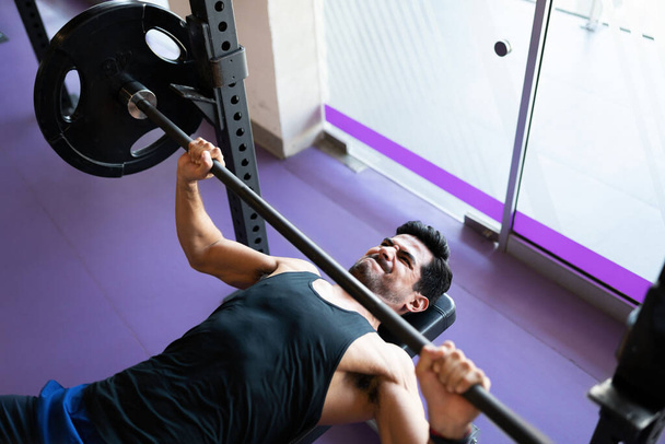 Jeune homme athlétique sur le point de soulever une barre de poids lourd au centre de fitness - Photo, image