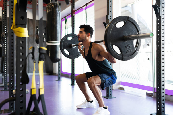 Beau jeune homme accroupi et se préparant à soulever des poids lourds à la salle de gym - Photo, image