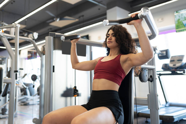 Giovane donna atletica e in forma con una pressa per le spalle presso il centro fitness - Foto, immagini