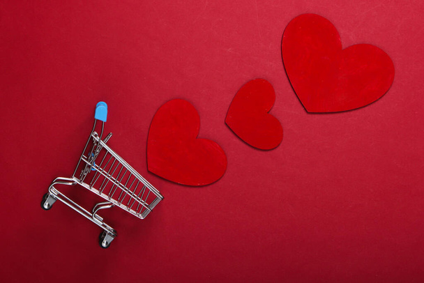 Mini supermarket trolley with red hearts on red background. Shopping lover concept - Photo, Image