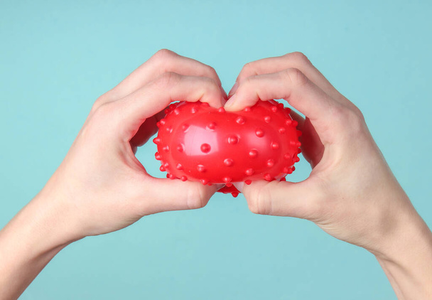 Hands holds a red massage ball on blue background. Antistress toy - Photo, Image